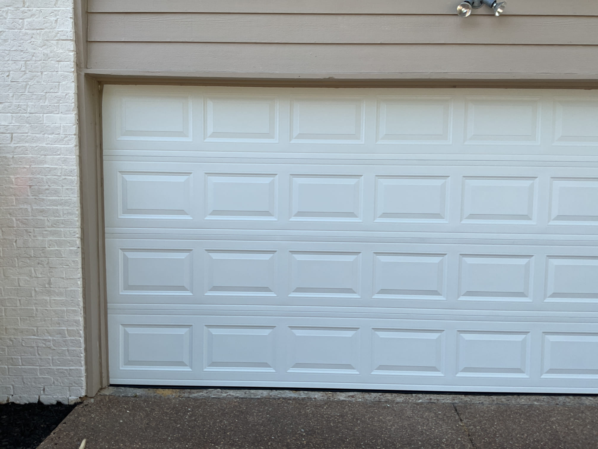 Angled exterior view of a finished white raised-panel garage door installation