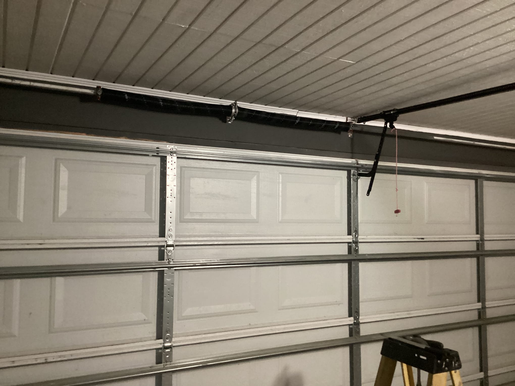 New torsion spring installed on the shaft above a white sectional garage door