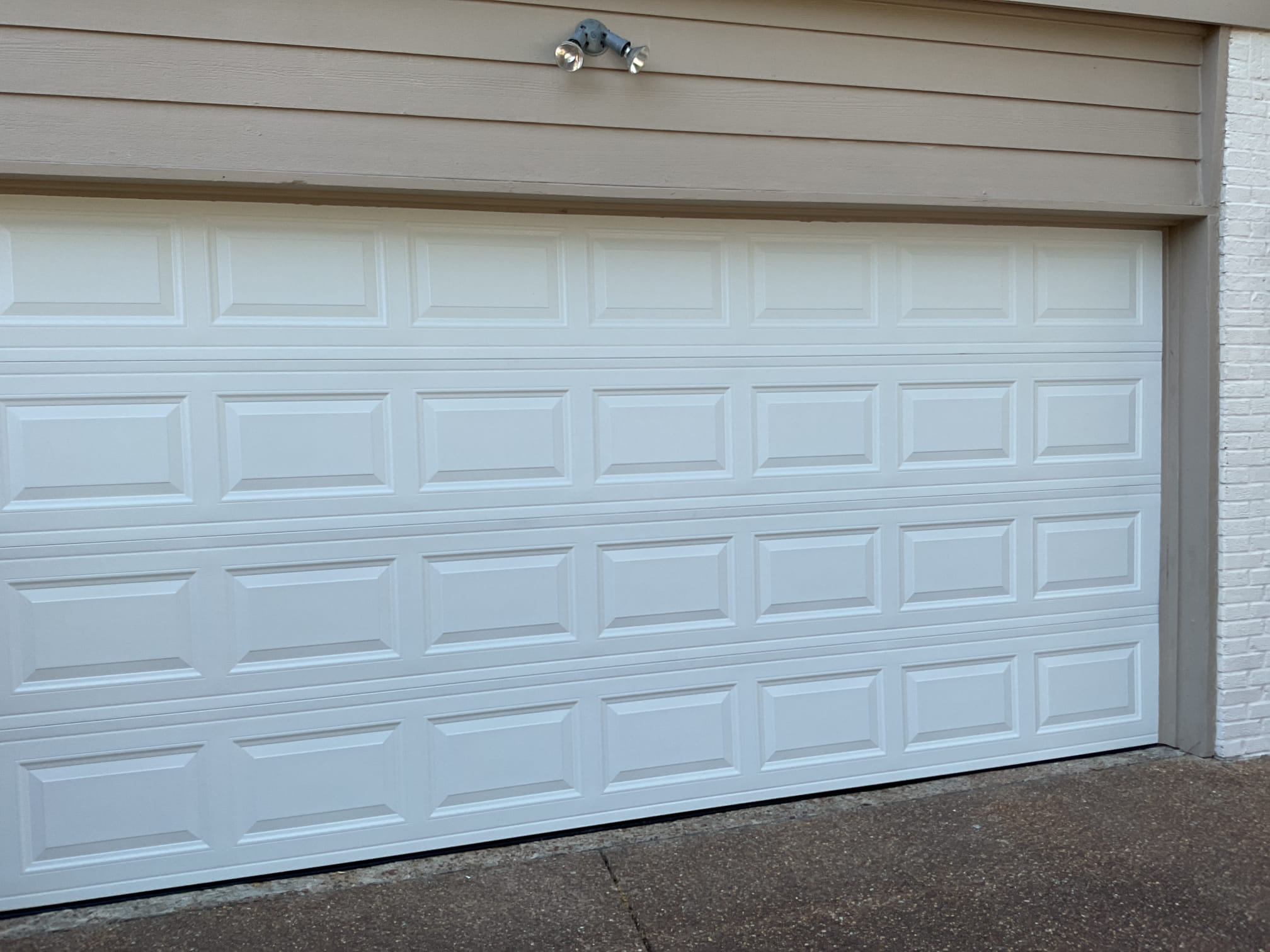 New white raised-panel double garage door installed beneath taupe siding