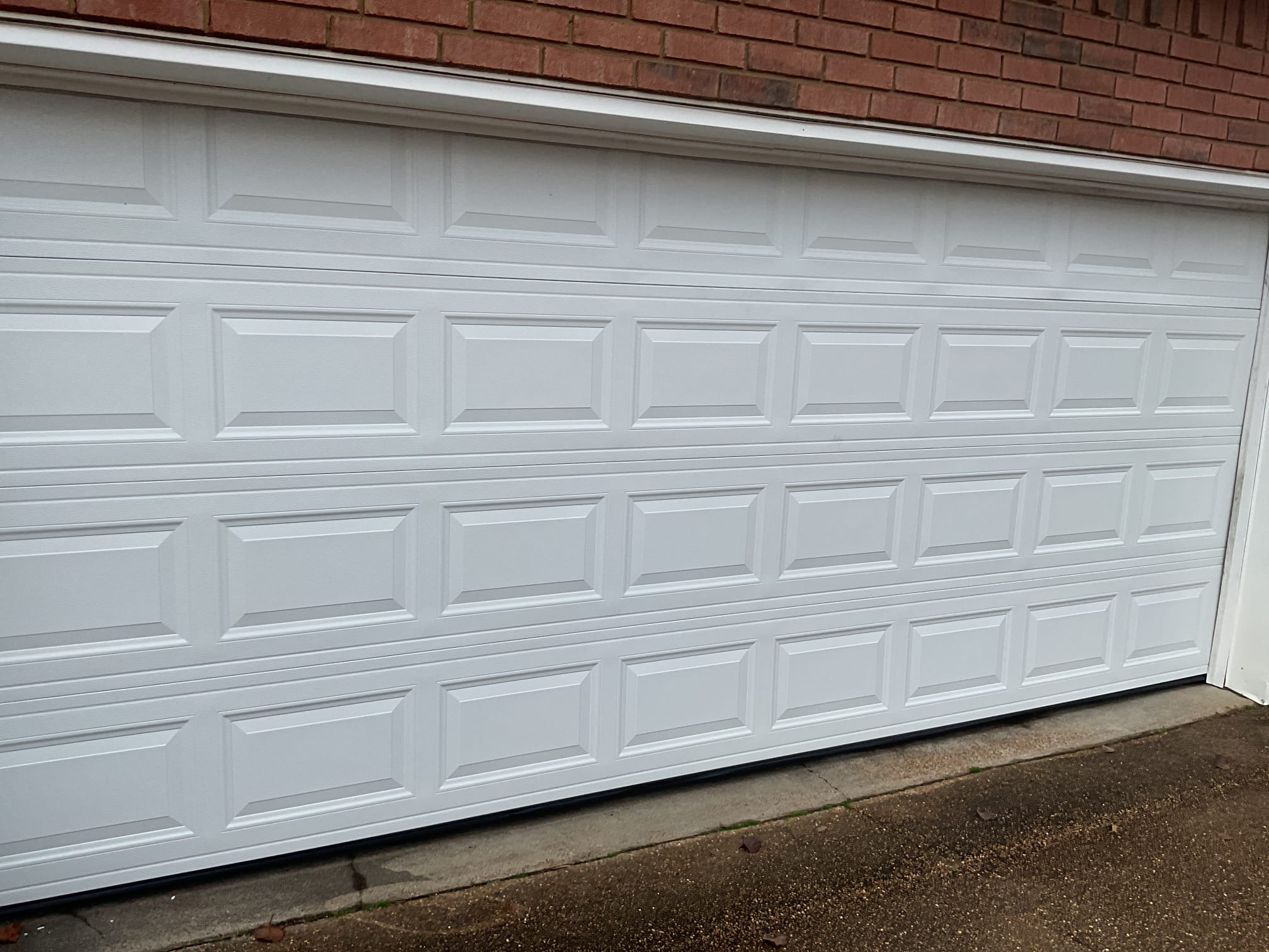 Finished white raised-panel garage door installed on a red brick home