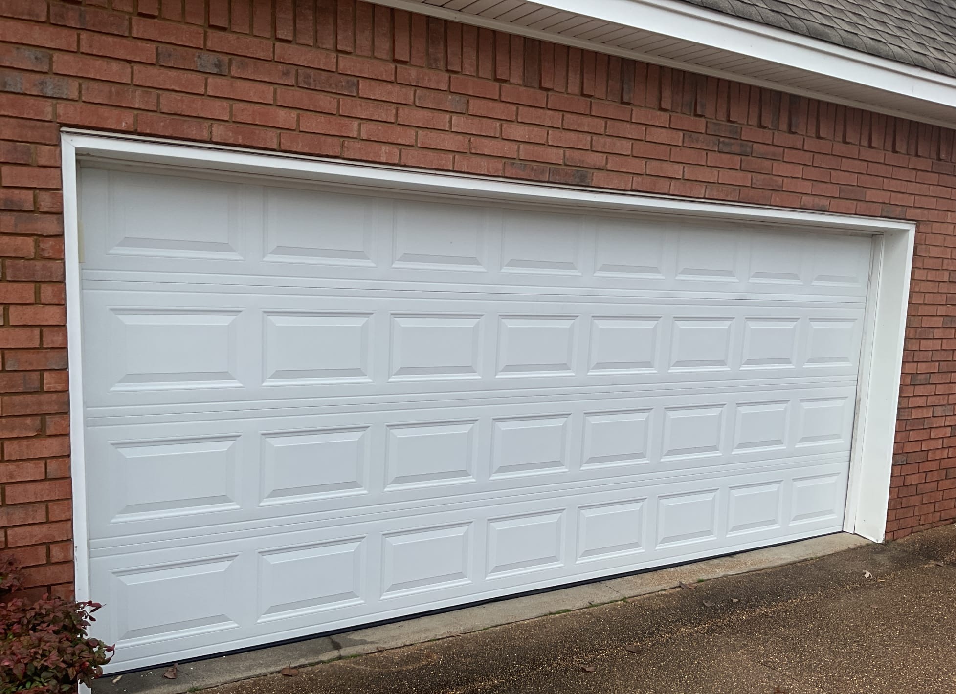 Second angle of a newly installed white raised-panel garage door on a brick home