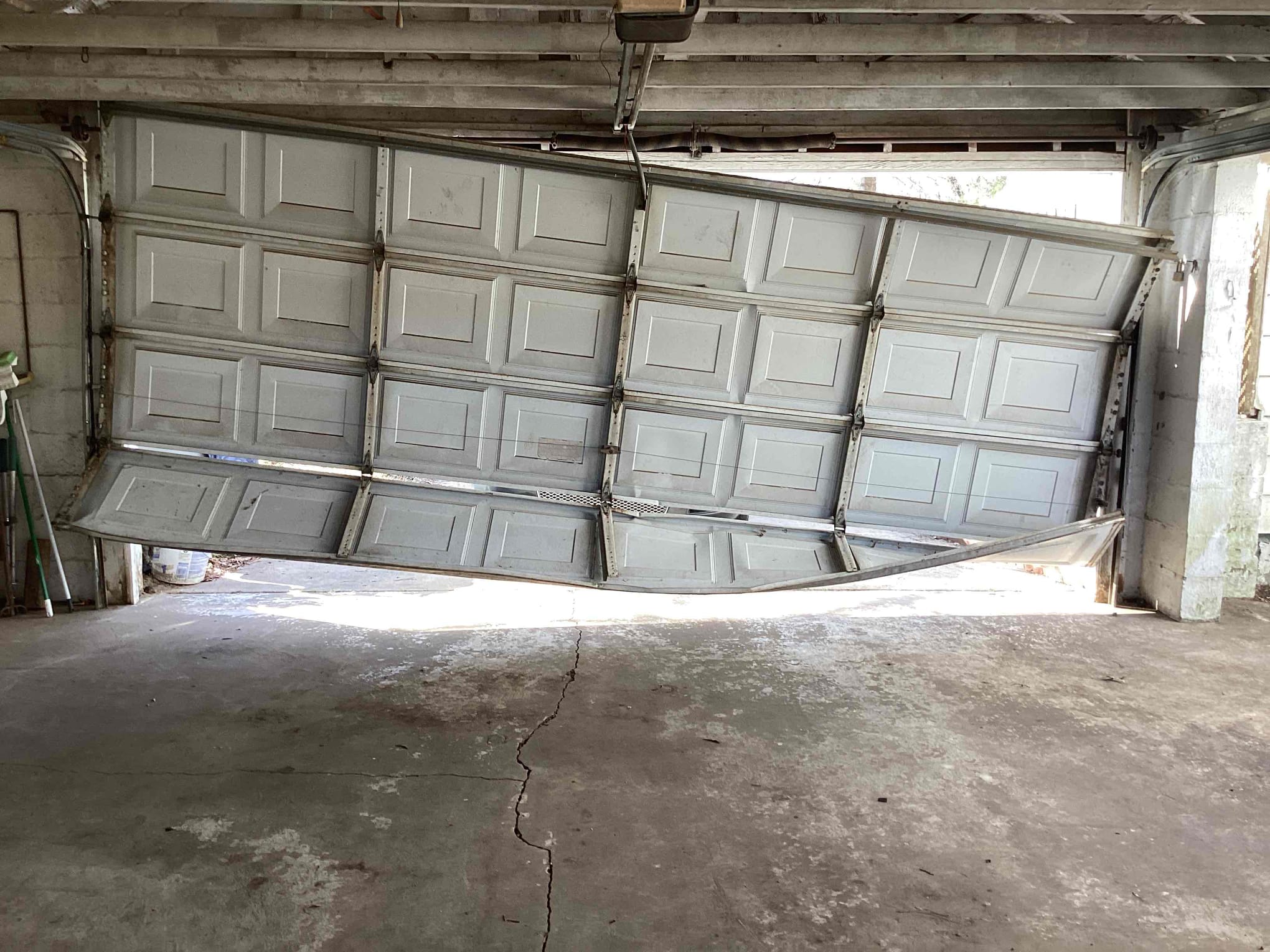 White garage door with a badly bowed and damaged bottom section spanning the width of the opening